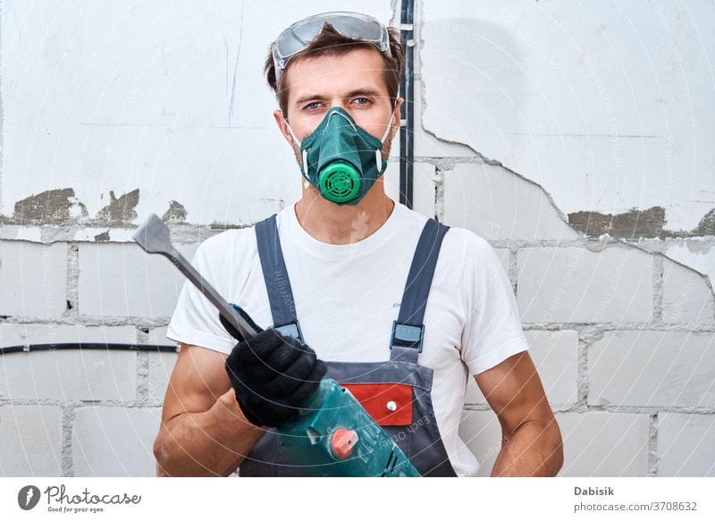 Renovation concept. Man in builder uniform with hammer drill make repairs in the room renovation man handyman protection construction male wall worker