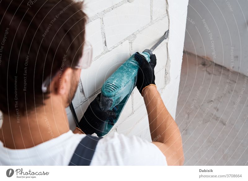 Man with demolition hammer removes stucco from wall. Concept of the renovation outline Hammer Drill by hand Construction Equipment work Tool Industry Machinery