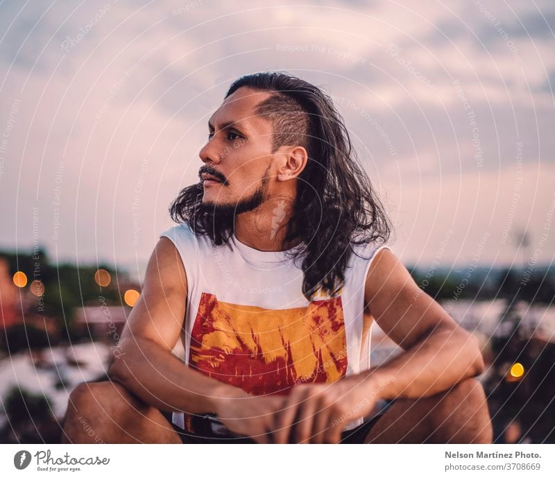 Portrait of hispanic male with long hair. We can see the city with a bokeh background. isolated person white adult proud front man casual lifestyle cool