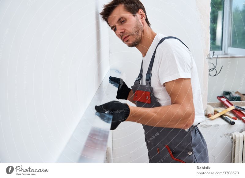 Renovation concept. Male worker plastering a wall using a long spatula renovation man tool stucco industry manual repair construction improvement home building