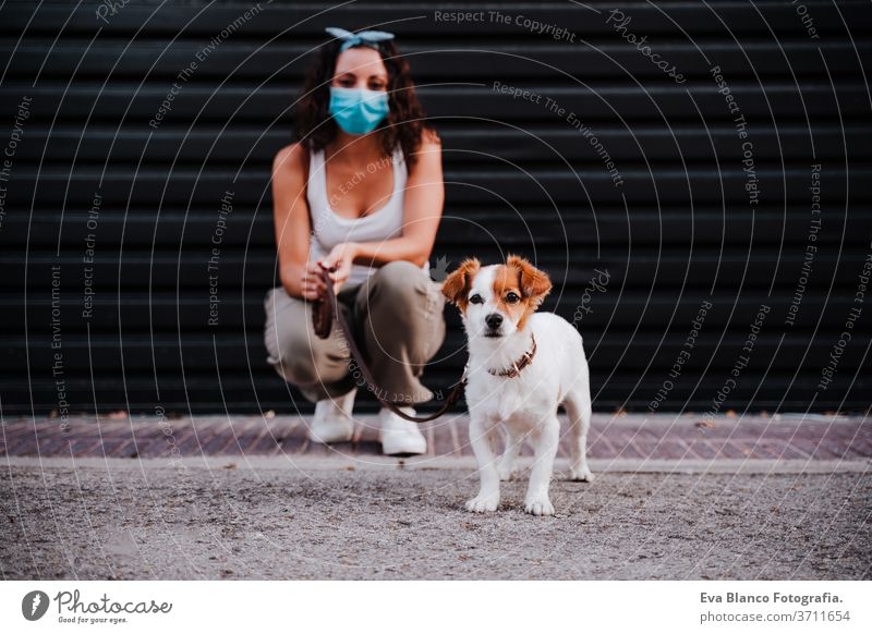 young woman outdoors wearing protective mask, cute jack russell dog besides. New normal concept street new normal pet walking urban city lifestyle corona virus