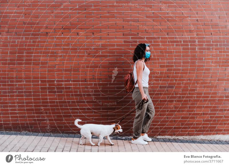 young woman walking outdoors wearing protective mask, cute jack russell dog besides. New normal concept street new normal pet urban city lifestyle corona virus