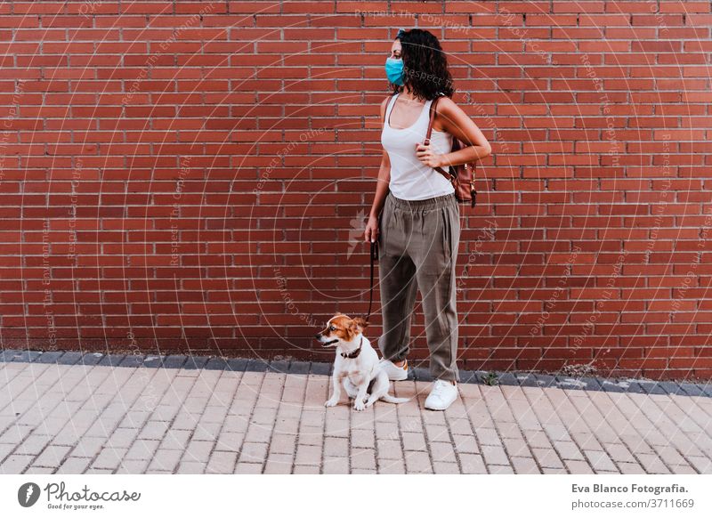 young woman walking outdoors wearing protective mask, cute jack russell dog besides. New normal concept street new normal pet urban city lifestyle corona virus