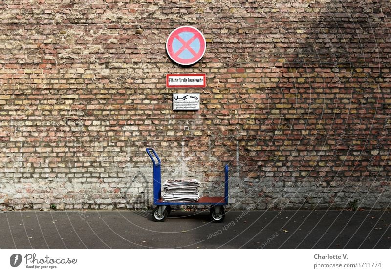 In the no stopping zone | handcart with newspapers in front of brick wall with no stopping sign Trolley transport trolley piles of newspapers Fire brigade area