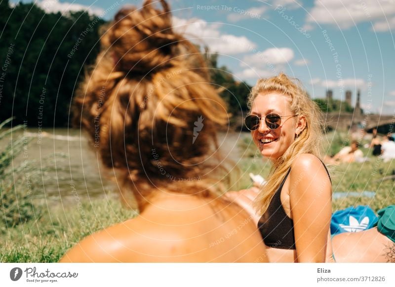 Two young women sunbathing and swimming at the Isar in Munich. One of them is blond, wears sunglasses and laughs. Summer. girlfriends Blonde sunbathe Good mood