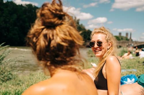 Two young women sunbathing and swimming at the Isar in Munich. One of them is blond, wears sunglasses and laughs. Summer. girlfriends Blonde sunbathe Good mood