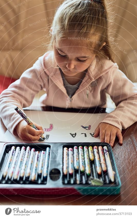 Little girl preschooler learning to write letters at home. Kid using crayons doing homework. Concept of early education attention caucasian child childhood cute
