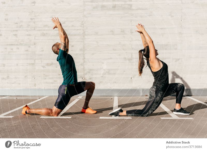 Fit couple doing yoga together in city crescent lunge pose practice asana anjaneyasana sportswear meditate healthy harmony wellness balance stretch flexible