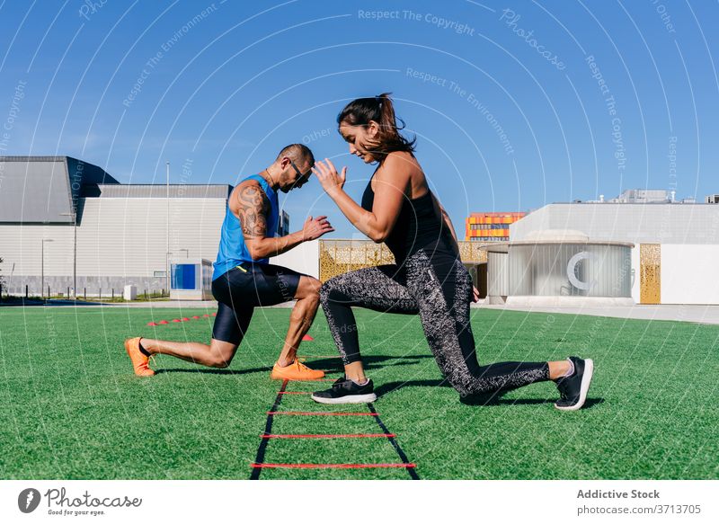 Athletic couple exercising with agility ladder on sports ground athlete training exercise equipment lunge together workout fitness activity sporty energy
