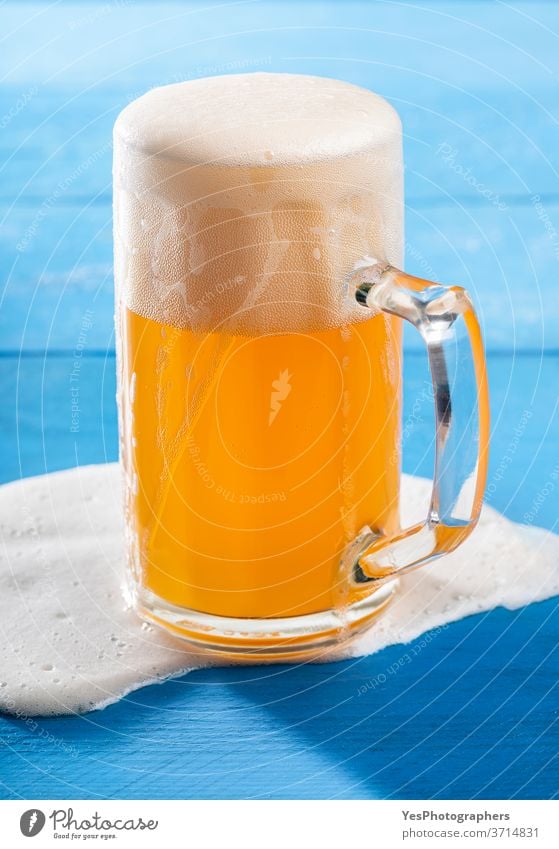 Pint of beer with spilled froth on blue table. German unfiltered beer Oktoberfest accident alcohol ale background bar bavarian beer foam beverage brew brewery