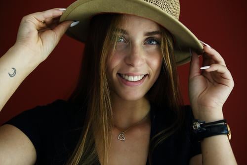 Direct portrait of a young woman in front of a red wall with a straw hat Athletic Feminine empathy Emotions emotionally Central perspective