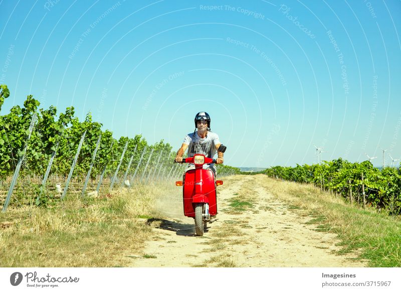 Riding a scooter in the vineyard. Man, with helmet riding scooter in the countryside. Portrait of a man and with a stylish vintage moped in summer against a blue sky