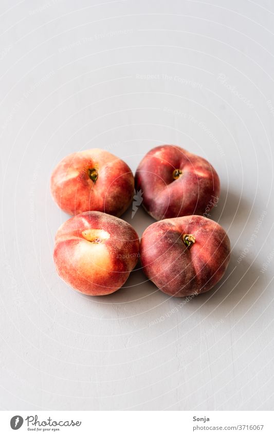 Four red flat peaches on a grey background in the middle Peach Red plane Gray Summer fruit Raw Juicy Sweet Fresh Mature Healthy Tasty natural Close-up Dessert