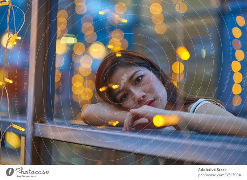 Thoughtful woman in cafe in evening thoughtful pensive city garland calm weekend window female asian ethnic lean relax rest tranquil peaceful style cozy trendy
