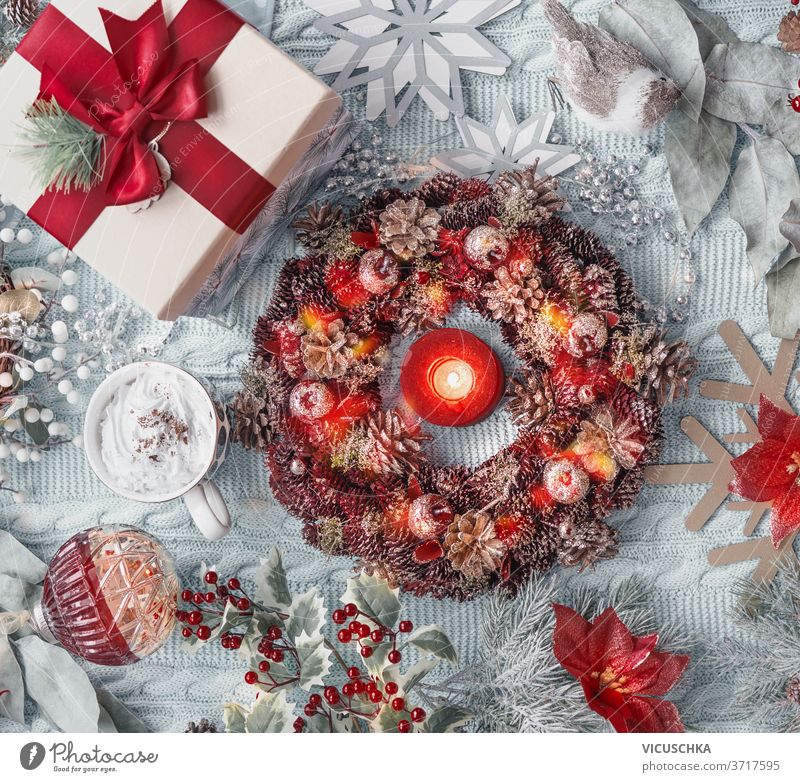 Christmas concept: advent wreath, present, hot chocolate in mug, Christmas flower, snowflakes, Christmas balls, and holly on light blue textile background. Top view