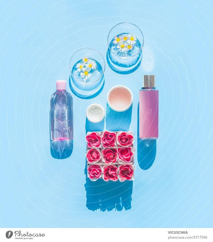Composition of natural cosmetic products and glasses with daisies, bottles, tubes and flowers on light blue background. Summer skin care concept. Top view . Spa or wellness