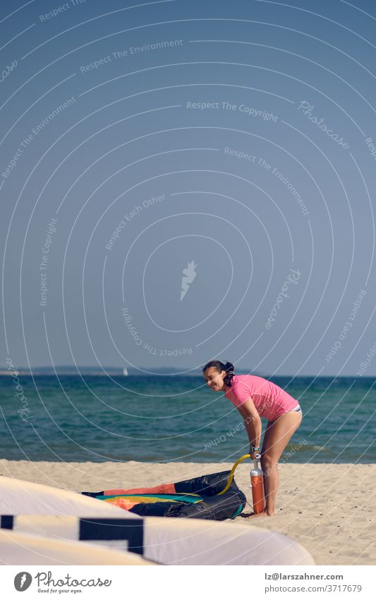 Middle-aged woman pumping up up a kitesurfing kite at the beach on summer vacation in hot sunshine with ocean backdrop middel-aged warm inflating kiteboarding