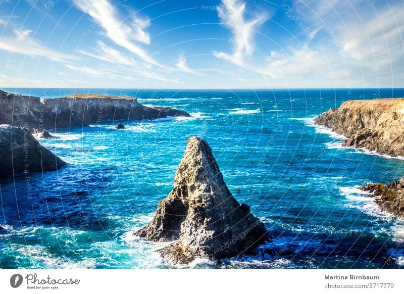 Cone shaped rock in the pacific ocean under a blue sky with clouds, California boulder california landscape travel shoreline beach cone stone water nature