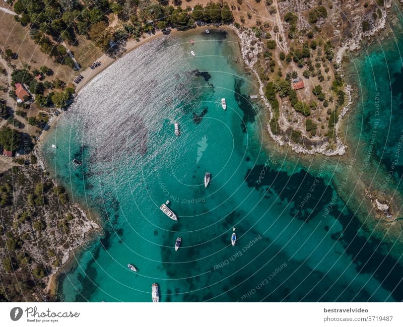 Mediterranean Greek landscape coastal drone shot with moored leisure boats. Aerial day top view of Sithonia Chalkidiki peninsula above shoreline with green plantation and crystal-clear calm sea.