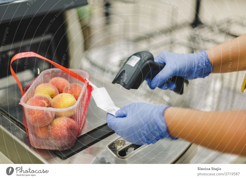 Scanning bar code. Woman or worker in blue medical gloves holding bar code scanner and scanning  paper on peach fruit. Shopping during the corona virus pandemic, selective focus