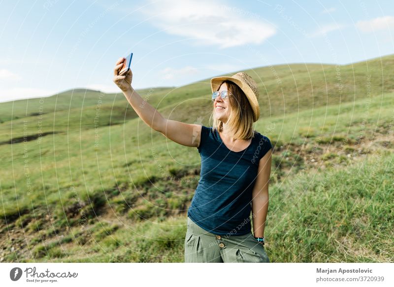 Young woman taking a selfie on hillside meadow in summertime adult adventure beautiful blog blogger blogging camera caucasian cheerful country cute enjoying