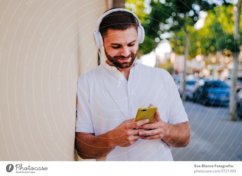 happy young man outdoors listening to music on mobile phone and headset. technology and lifestyle city urban smiling street modern beautiful summer using