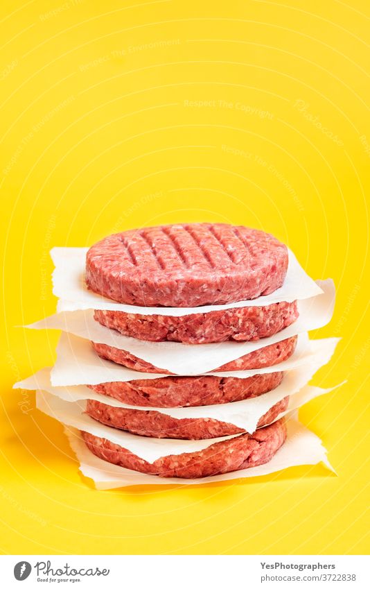 Burger patties stacked on the table. Raw beef patties isolated on yellow background. barbeque bbq burger butcher close-up comfort food cooking cow meat cuisine