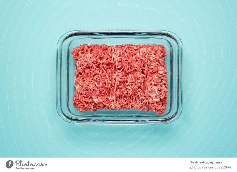 Raw beef in a glass food container. Ground meat in glass dish isolated on a colored background above view blue bowl box burger cooking cow meat cuisine culinary