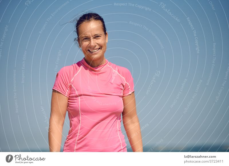 Happy smiling attractive athletic slender middle-aged woman looking down at the camera with a warm friendly smile against a sunny blue summer sky with copy space