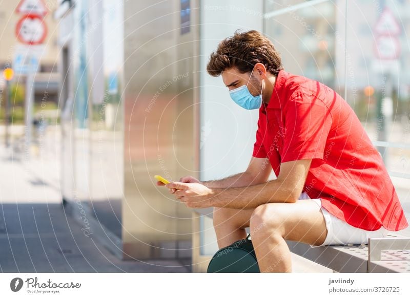 Young man wearing a surgical mask while waiting for a train at an outside station student tourism ecomobility traveler young male backpack lifestyle person