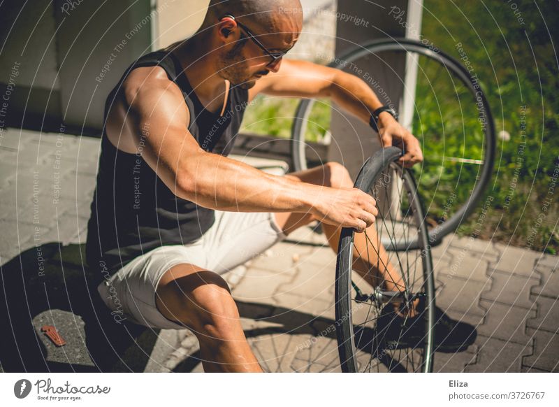 A man sits outside in the sun and pulls a bicycle coat onto the wheel of his bicycle after he has patched the tube Bicycle repair Coat Hose impeller wind Sun
