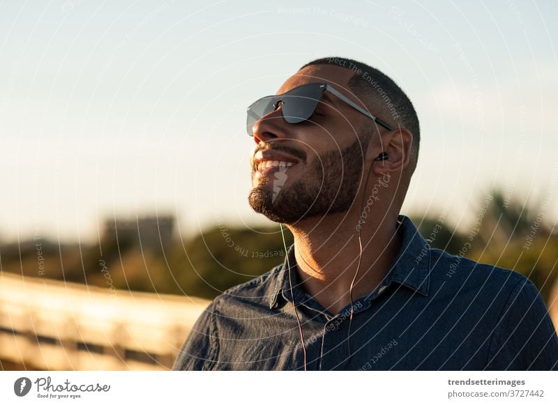 Latin man using earphones to listen music or motivational podcasts and enjoying the sunset meditation moutains vacation beach outside sunny mountains happy
