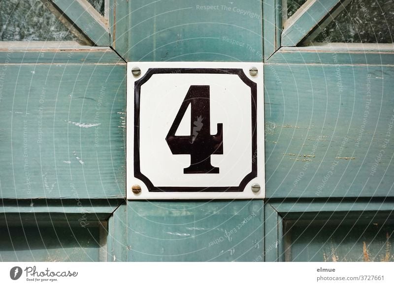 The number four is in black and framed on a square shield on the old blue wooden door 4 sign Number plate Old building front door Wooden door dwell