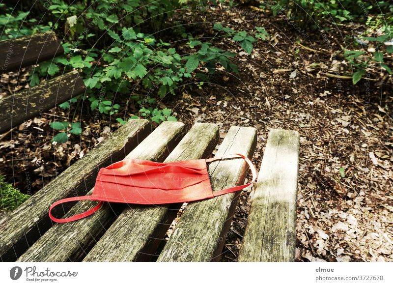 a red nose-mask lies on an old wooden bench in the forest Nose and mouth mask Mask Refusal Corona virus Risk of infection Respirator mask Wooden bench Face mask