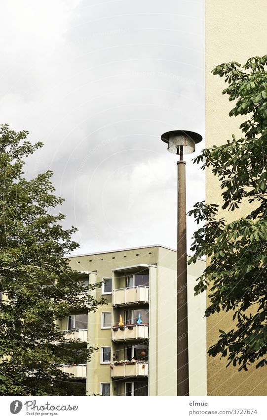 Holidays on balconies - view of a renovated modern apartment building with individually designed balconies, past a street lamp, a house wall and two trees