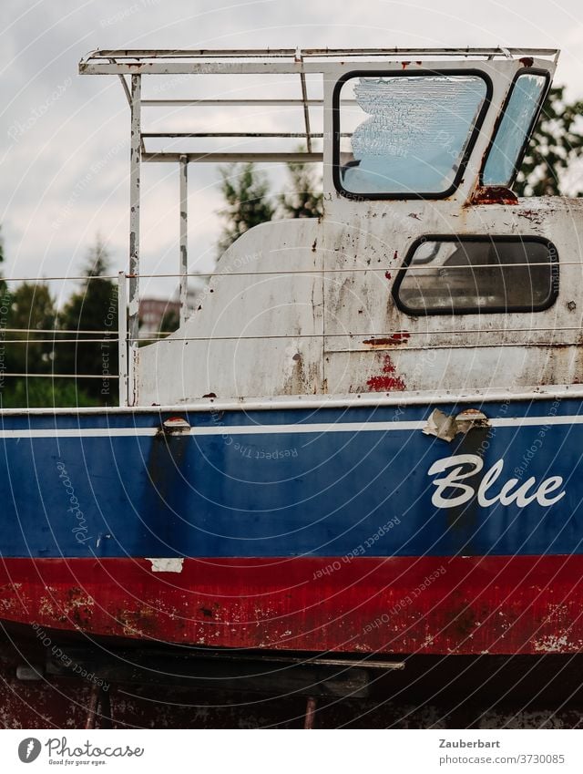 Blue - side view and bridge of an old motorboat in red and blue Old Red White Stern Rust corroded warehouse Boat storage Buck jacked up ship ship graveyard Oar