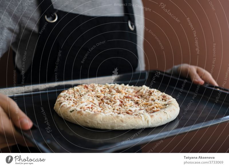 Woman holding oven tray with frozen pizza food uncooked comfort food fast food snack calories quick cheese dinner lunch mozzarella appetizing cold woman apron