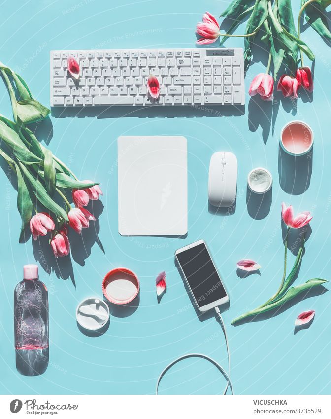 Spring concept . Smartphone mock up. PC keyboard, tulips and natural cosmetic products. Light blue background. Lifestyle beauty blogging concept. Flat lay. Top view