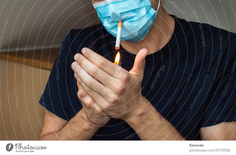Man lighting a cigarette while wearing face mask. Covid funny concept coronavirus covid 19 man person smoke leisure home party drug addiction strange rare fail