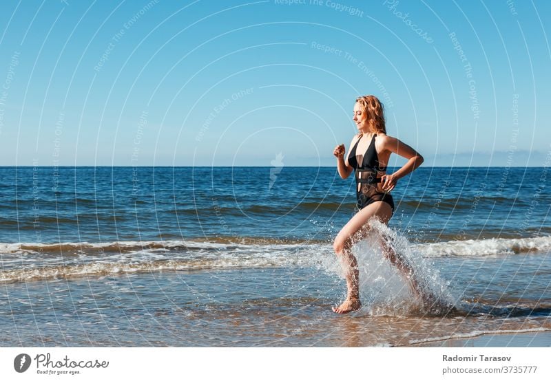 young blonde girl in a black swimsuit runs along the sand of the sea shore  - a Royalty Free Stock Photo from Photocase