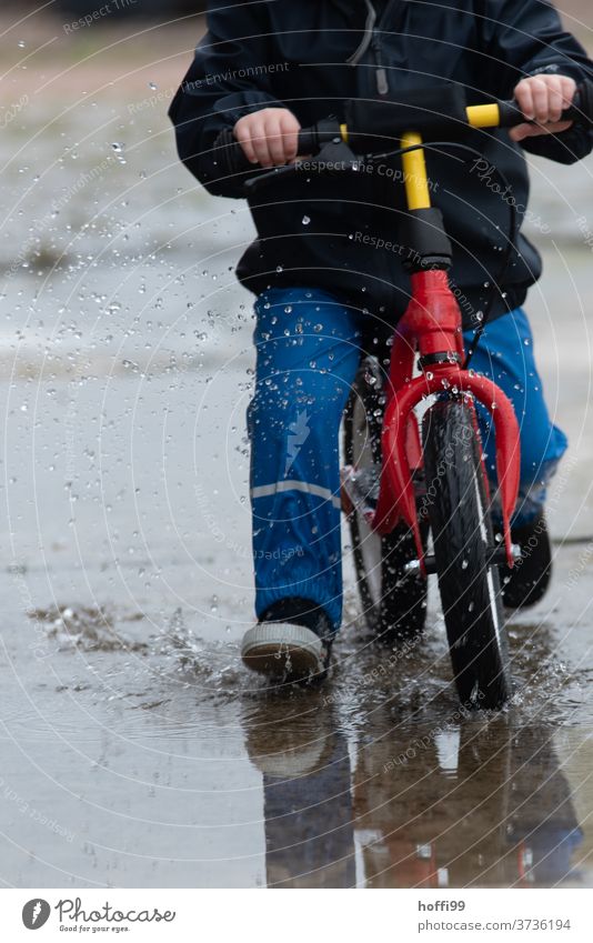 Child on a running bike rides through the puddle with a swing impeller Children's game Toddler Puddle puddle picture Inject Drops of water Wet Water Playing