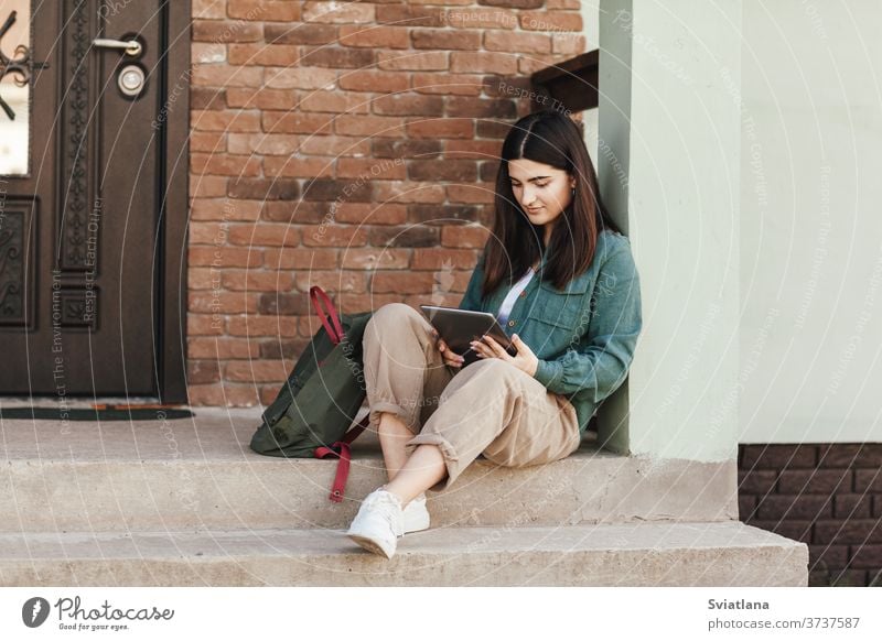 Young female student sitting on steps and studying with tablet in college or private school, technology teaching concept. Technology, education, leisure concept