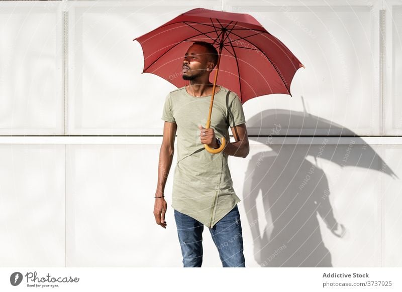 Ethnic man on sunny day on street enjoy summer city umbrella hide relax calm serene urban male ethnic black african american building stand rest handsome trendy