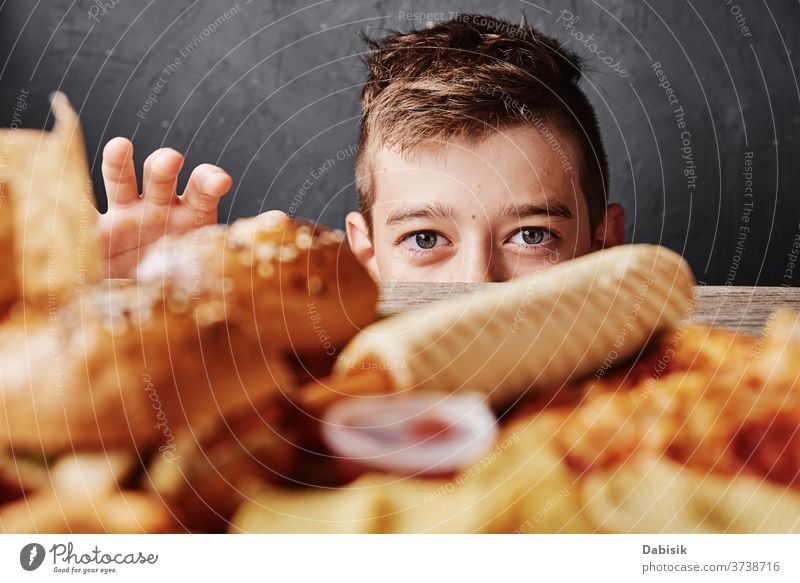 Hungry boy looks at tasty food and take a hamburger from table. Unhealthy food concept fat diet pizza background cholesterol cheeseburger restaurant catering