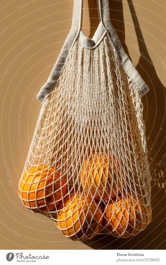 Ripe oranges in a white string bag. Beige background. zero waste eco shopping beige reusable concept ecology cotton market vegetarian no plastic economical