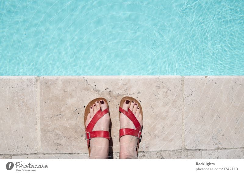 Feet in red sandals by the edge of a swimming pool color colorful pair space sun leisure shoe footwear fashion feet background bare blue bright concept feel