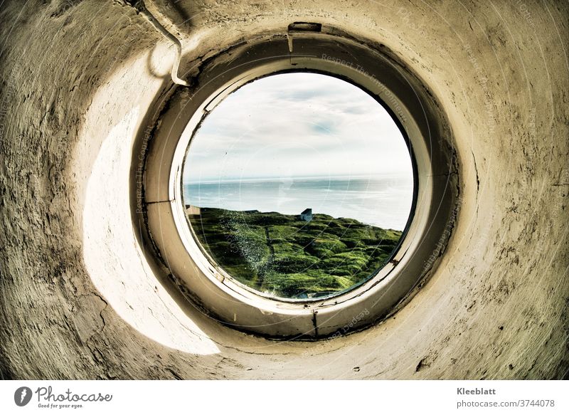 Through a round porthole of the lighthouse the view to the sea Lighthouse round window Porthole roughly plastered wall grey-white colour old parent