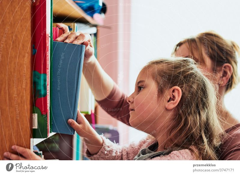 Little girl preschooler choosing a book to read reading bookshelf library bookcase looking education finding choose childhood lifestyle home searching picking