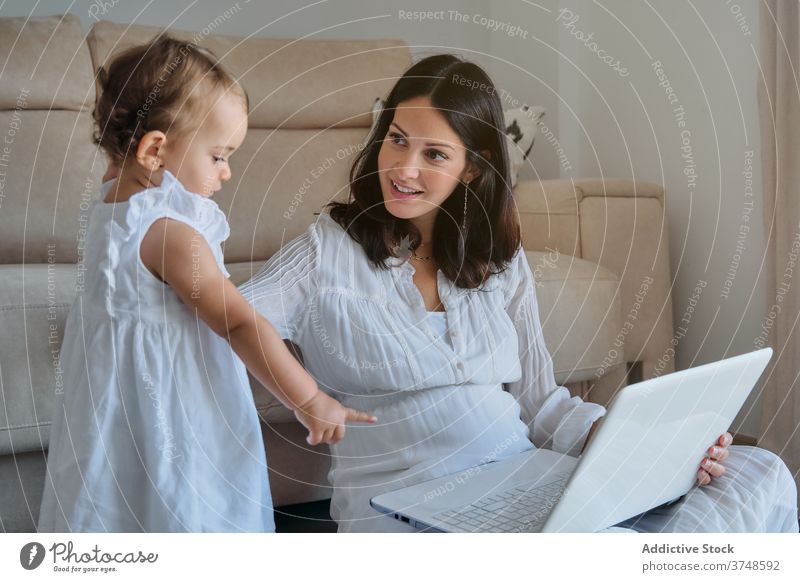 Little girl pointing to a laptop held by her mother sitting on the floor innocence lifestyles share homework togetherness bonding desire freelance learn