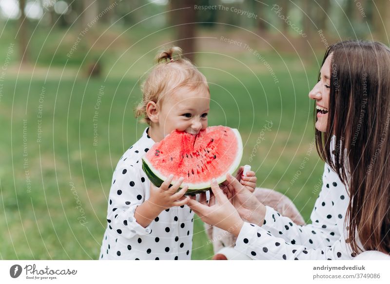 happy mother and daughter eat watermelon in summer park. Happy smiling family eating watermelon in park. Mother and daughter spend time together. Diet, vitamins, healthy food concept. selective focus